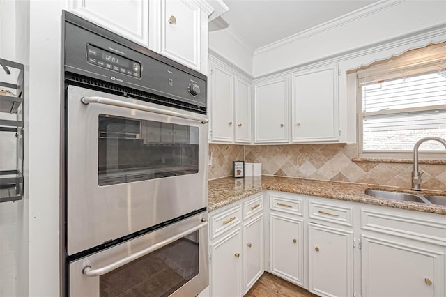 kitchen featuring light stone counters, white cabinetry, double oven, ornamental molding, and sink