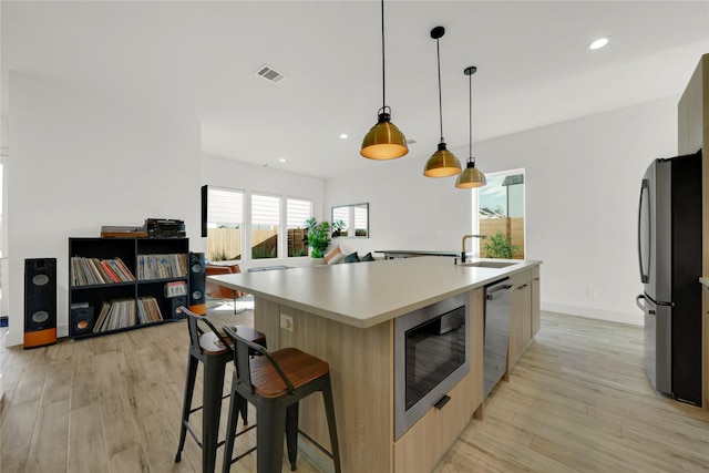 kitchen with decorative light fixtures, a center island with sink, appliances with stainless steel finishes, and a healthy amount of sunlight