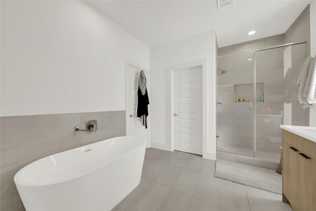 bathroom with independent shower and bath, tile patterned flooring, tile walls, and vanity