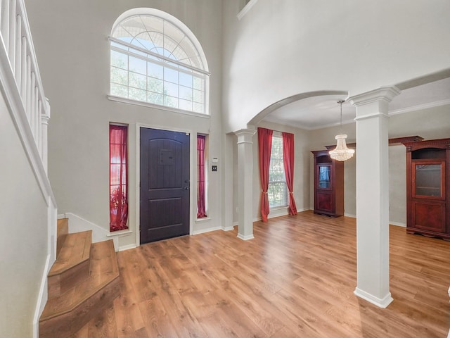 foyer with plenty of natural light, a towering ceiling, light hardwood / wood-style flooring, and ornate columns