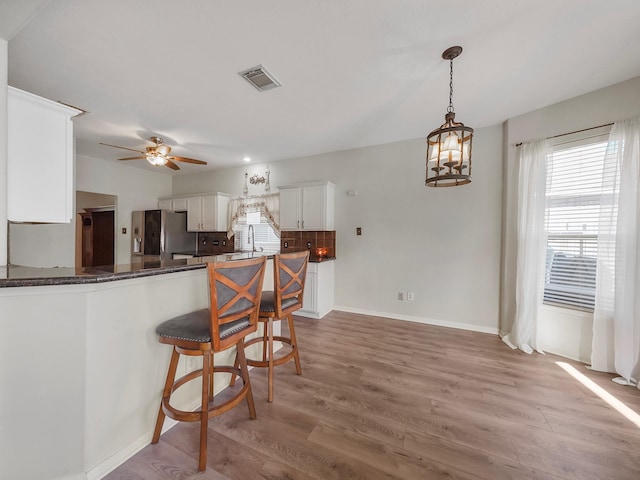 kitchen featuring white cabinets, hardwood / wood-style floors, tasteful backsplash, kitchen peninsula, and stainless steel fridge