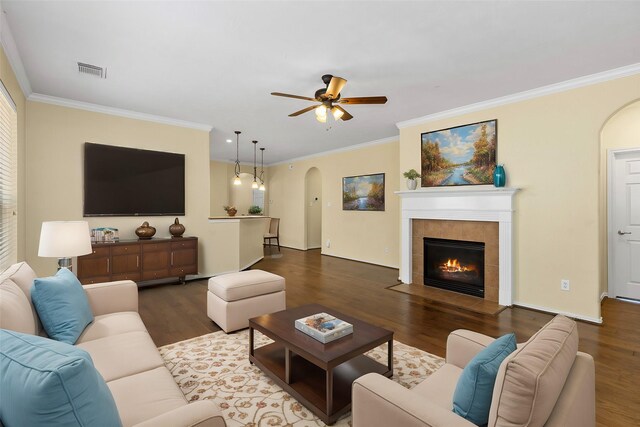 living room with ceiling fan, wood-type flooring, a tile fireplace, and ornamental molding