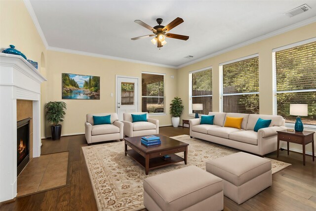 living room featuring ceiling fan, hardwood / wood-style floors, crown molding, and a tiled fireplace