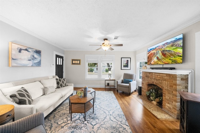 living room with a brick fireplace, hardwood / wood-style floors, crown molding, and ceiling fan