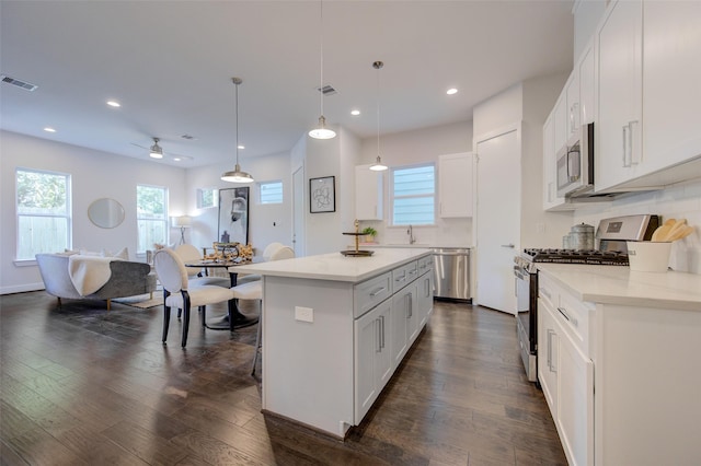 kitchen featuring appliances with stainless steel finishes, a center island, ceiling fan, pendant lighting, and white cabinetry