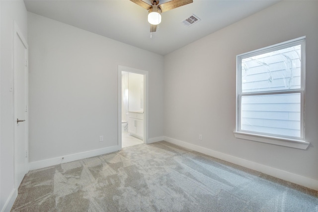 unfurnished bedroom featuring ensuite bathroom, light colored carpet, and ceiling fan