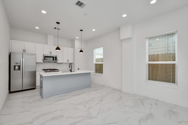 kitchen featuring a kitchen island with sink, stainless steel appliances, pendant lighting, white cabinetry, and backsplash