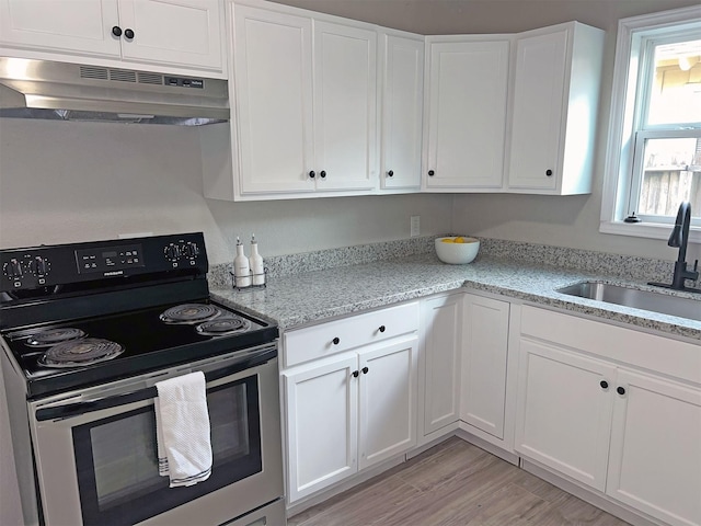 kitchen with light stone counters, light hardwood / wood-style floors, electric range, white cabinetry, and sink