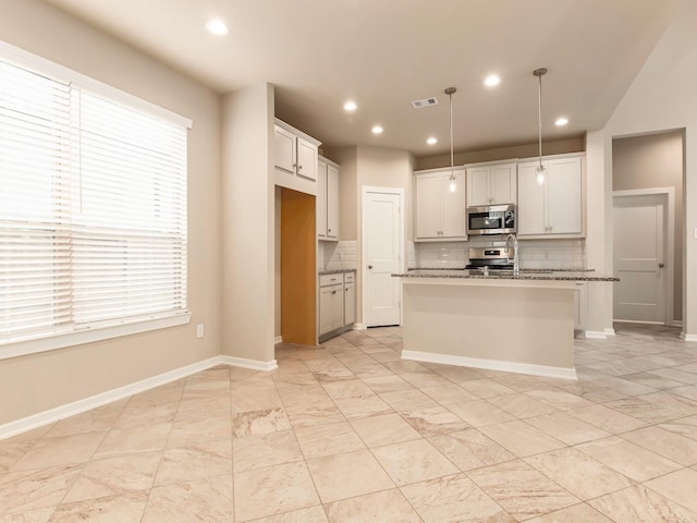 kitchen featuring light stone countertops, hanging light fixtures, a kitchen island with sink, white cabinets, and appliances with stainless steel finishes