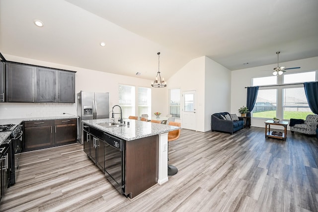 kitchen featuring light stone counters, a center island with sink, decorative backsplash, black dishwasher, and sink