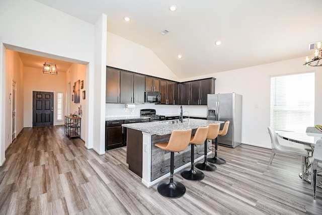 kitchen with stainless steel appliances, an island with sink, light stone countertops, a breakfast bar, and decorative backsplash