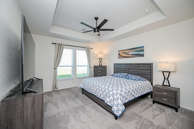 carpeted bedroom featuring ceiling fan and a tray ceiling