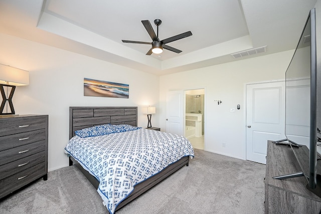 carpeted bedroom with ensuite bathroom, ceiling fan, and a tray ceiling