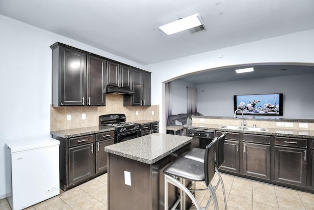 kitchen featuring light tile patterned floors, black appliances, a kitchen island, a kitchen breakfast bar, and sink