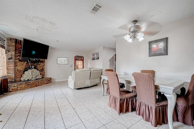 tiled dining space featuring a textured ceiling, ceiling fan, and a large fireplace