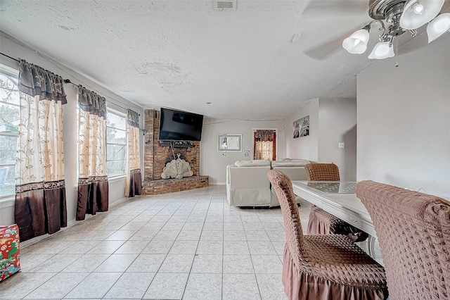 tiled living room with a textured ceiling, ceiling fan, and a fireplace