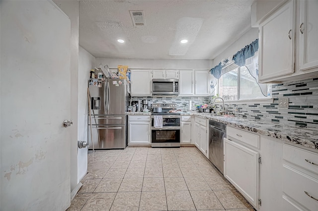 kitchen featuring a textured ceiling, appliances with stainless steel finishes, light tile patterned floors, and white cabinetry