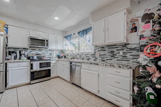 kitchen featuring appliances with stainless steel finishes, sink, white cabinetry, light tile patterned flooring, and tasteful backsplash