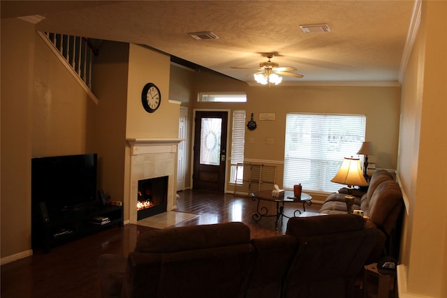 living room with a tile fireplace, hardwood / wood-style floors, ceiling fan, crown molding, and a textured ceiling