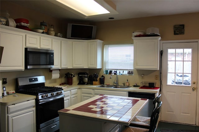 kitchen with sink, appliances with stainless steel finishes, white cabinetry, a center island, and tile counters