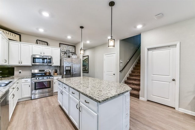 kitchen featuring decorative light fixtures, light hardwood / wood-style floors, a kitchen island, stainless steel appliances, and white cabinets