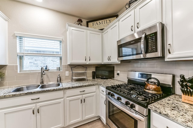 kitchen featuring white cabinetry, appliances with stainless steel finishes, tasteful backsplash, light stone counters, and sink