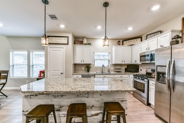 kitchen with appliances with stainless steel finishes, hanging light fixtures, a kitchen island, white cabinets, and sink