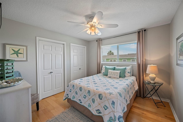 bedroom with a textured ceiling, ceiling fan, light hardwood / wood-style floors, and multiple closets