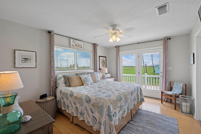 bedroom featuring ceiling fan, light hardwood / wood-style floors, a textured ceiling, and access to exterior