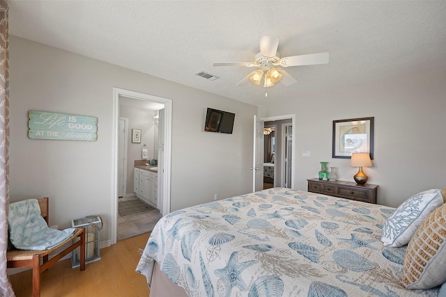 bedroom with ceiling fan, light wood-type flooring, ensuite bath, and a textured ceiling