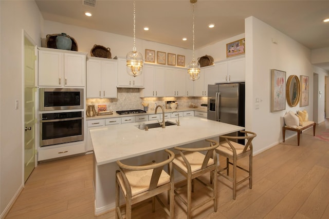 kitchen featuring appliances with stainless steel finishes, an island with sink, pendant lighting, white cabinets, and sink