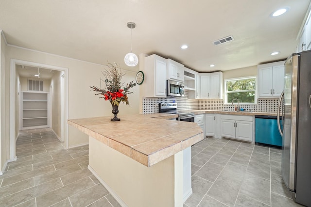 kitchen featuring hanging light fixtures, stainless steel appliances, kitchen peninsula, white cabinetry, and tasteful backsplash