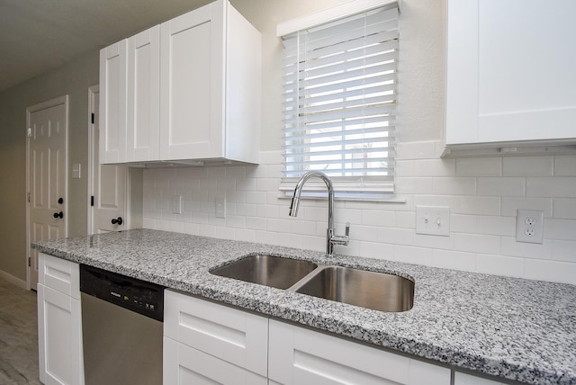 kitchen featuring sink, white cabinets, light stone counters, stainless steel dishwasher, and backsplash