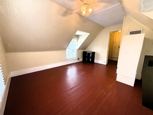 bonus room featuring lofted ceiling, wood walls, ceiling fan, and dark wood-type flooring