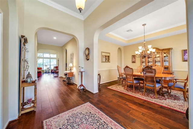 dining room with a raised ceiling, crown molding, an inviting chandelier, and dark hardwood / wood-style flooring