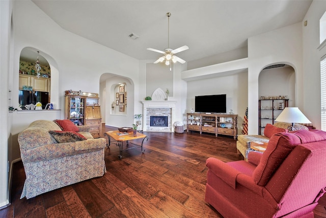 living room with wood-type flooring, a stone fireplace, a towering ceiling, and ceiling fan