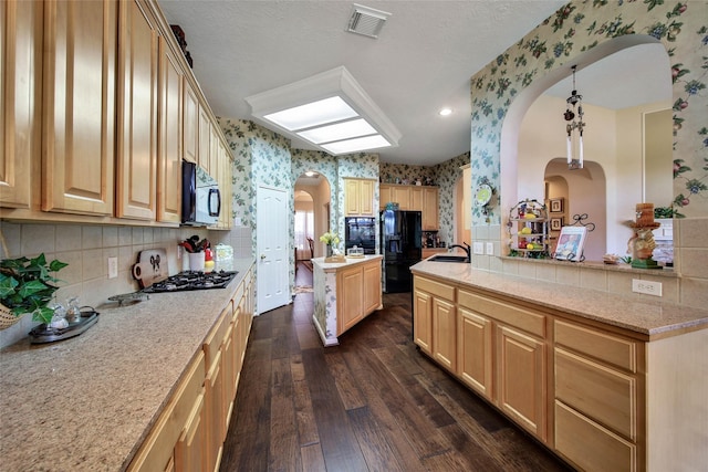 kitchen featuring hanging light fixtures, a center island, black appliances, dark wood-type flooring, and light brown cabinets