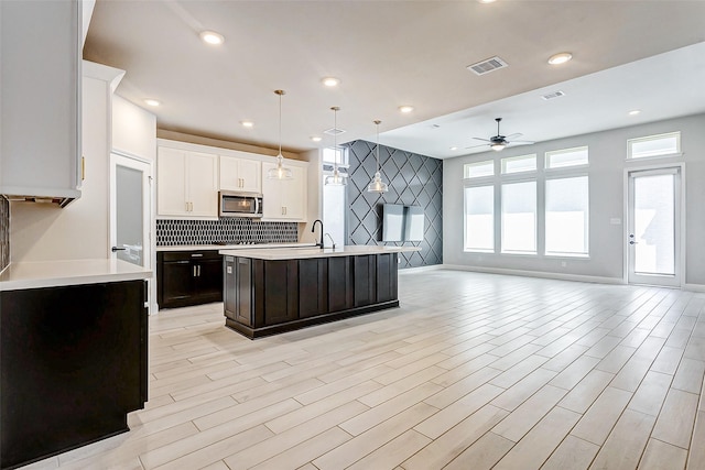 kitchen featuring white cabinets, ceiling fan, hanging light fixtures, dark brown cabinetry, and a kitchen island with sink