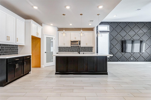 kitchen with decorative light fixtures, white cabinets, a center island with sink, and backsplash