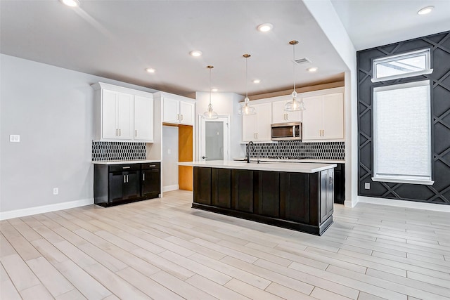 kitchen with hanging light fixtures, a center island with sink, light wood-type flooring, white cabinets, and sink