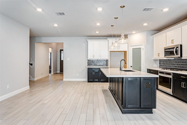 kitchen with stainless steel appliances, sink, white cabinetry, hanging light fixtures, and a center island with sink