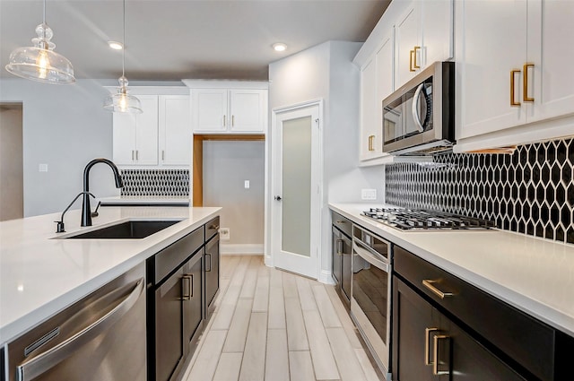 kitchen with appliances with stainless steel finishes, pendant lighting, decorative backsplash, white cabinets, and sink