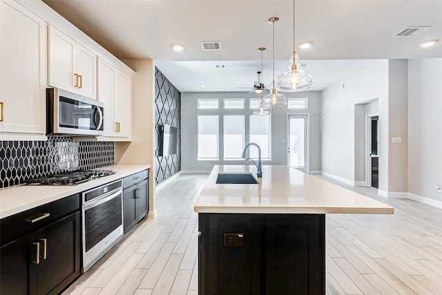 kitchen with hanging light fixtures, an island with sink, white cabinets, appliances with stainless steel finishes, and sink