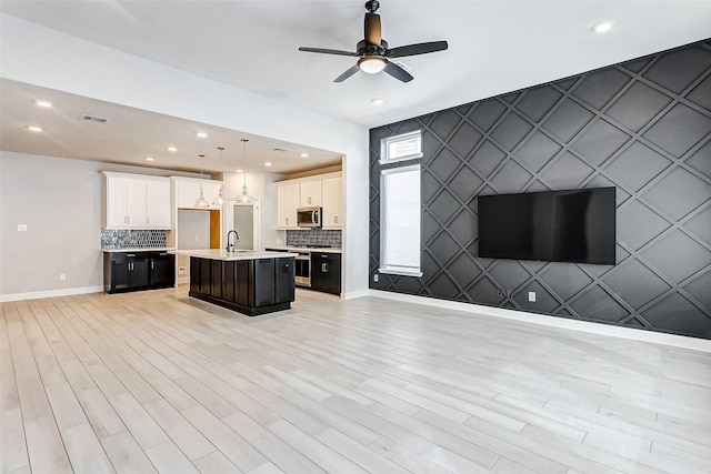 kitchen featuring pendant lighting, an island with sink, white cabinetry, ceiling fan, and sink