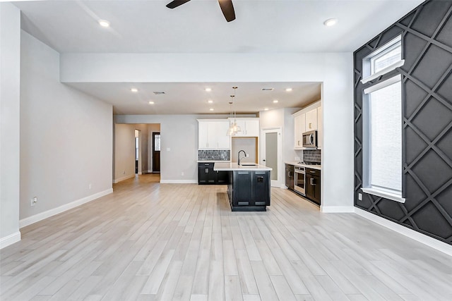 kitchen with an island with sink, pendant lighting, decorative backsplash, white cabinetry, and stove