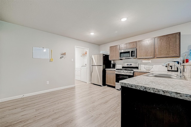 kitchen featuring washer and clothes dryer, stainless steel appliances, light hardwood / wood-style floors, backsplash, and sink