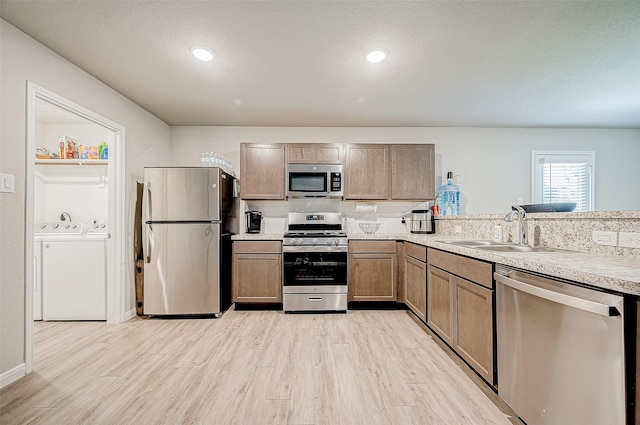 kitchen with appliances with stainless steel finishes, light hardwood / wood-style flooring, washer and clothes dryer, and sink