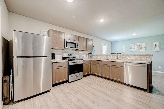 kitchen featuring stainless steel appliances, kitchen peninsula, sink, light hardwood / wood-style flooring, and backsplash