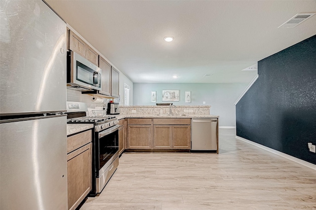 kitchen featuring kitchen peninsula, stainless steel appliances, tasteful backsplash, light wood-type flooring, and sink