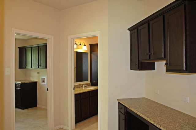 kitchen featuring a sink, dark brown cabinets, light stone counters, and light tile patterned flooring